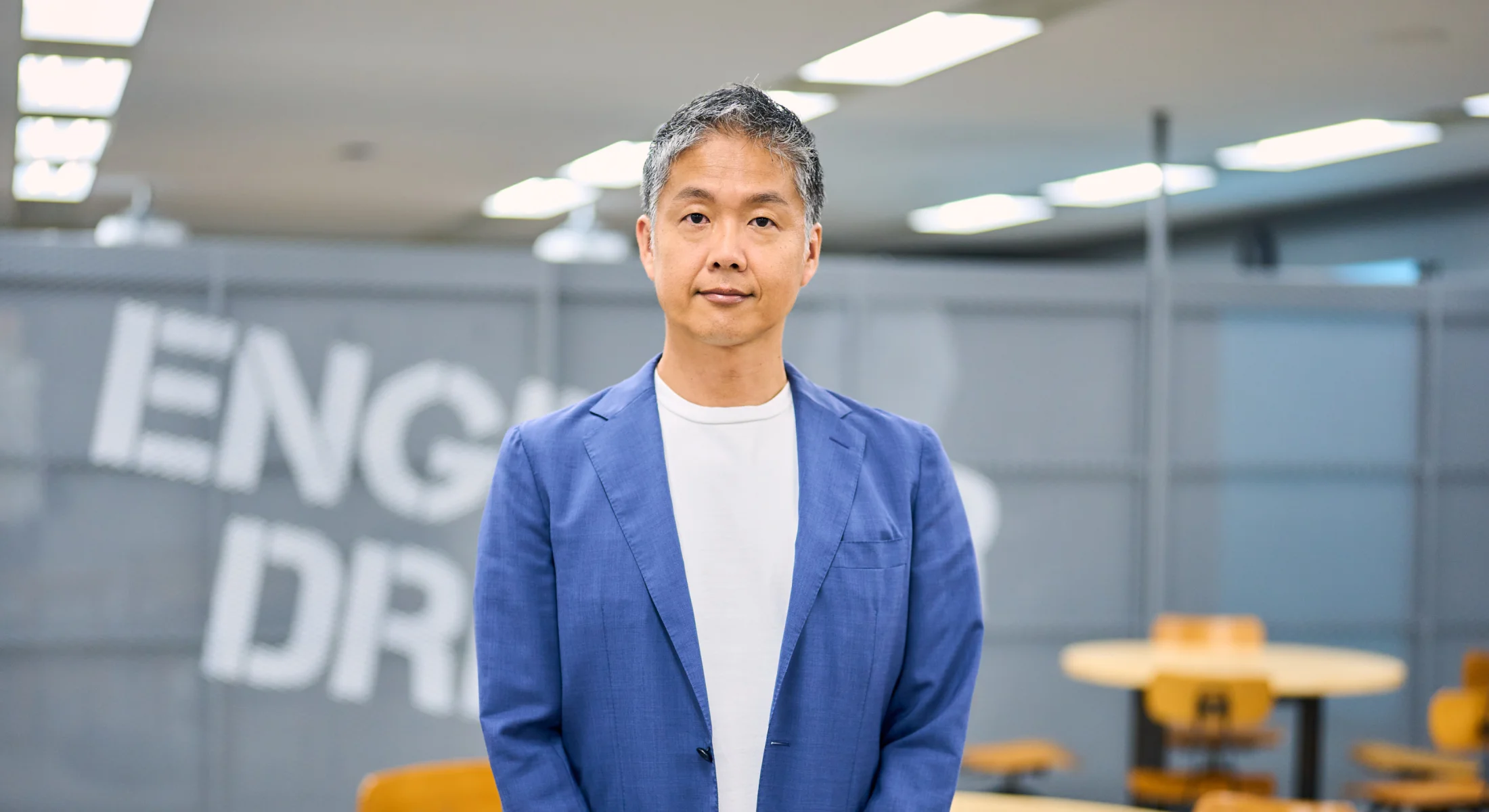 オフィスの壁面ロゴの前に立つ取締役 副社長
